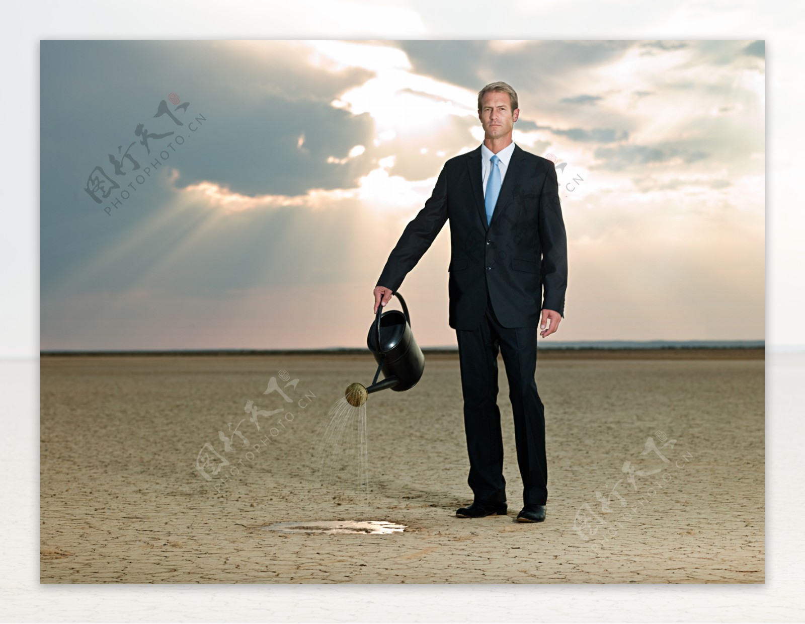 提着水壶在沙漠中浇水的外国商业男人图片
